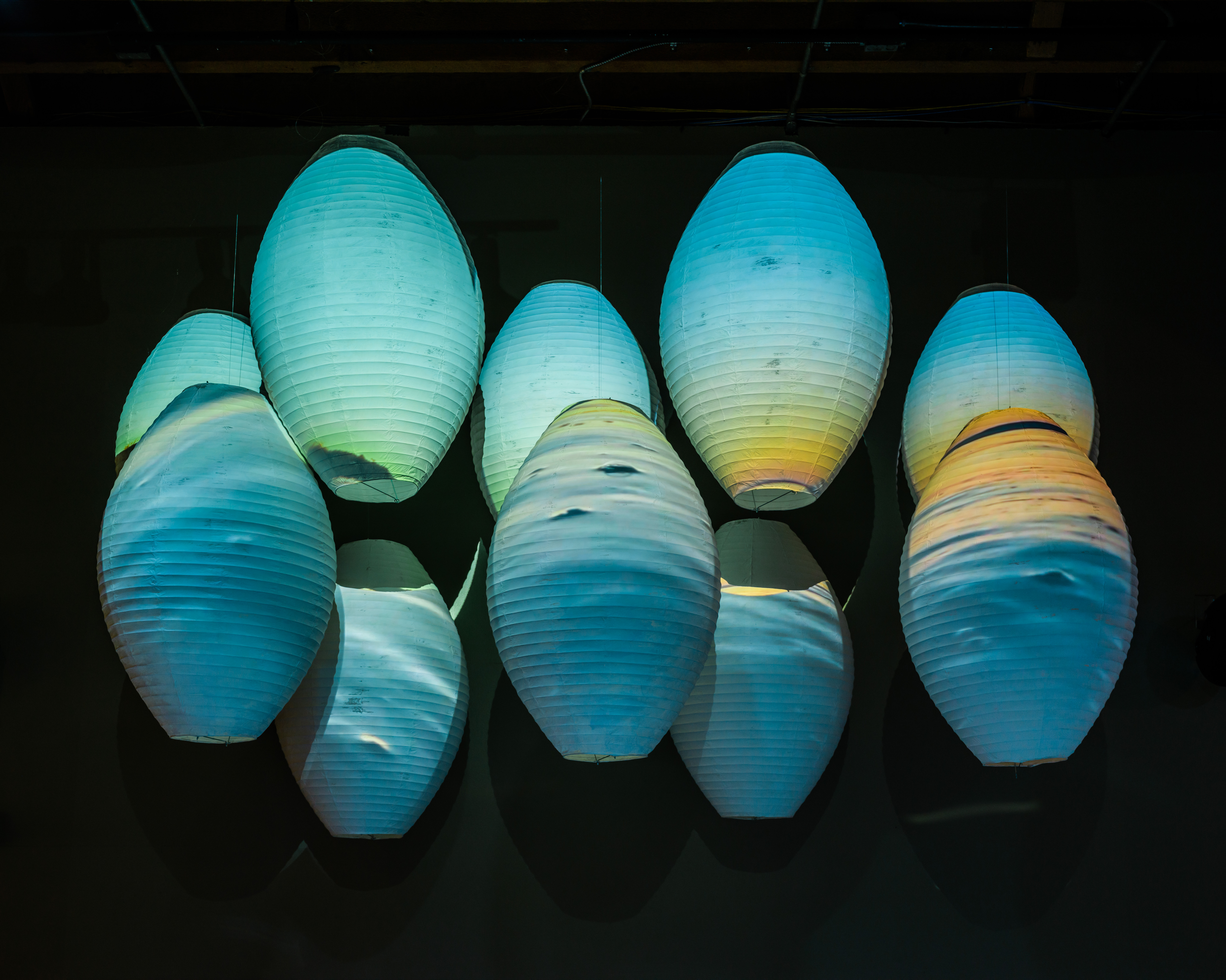 Blue and orange gradients projected onto 10 egg-shaped hanging sculptures